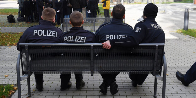 Vier Polizeischüler sitzen mit dem Rücken zum Betrachter auf einer Bank Vier Polizeischüler sitzen mit dem Rücken zum Betrachter auf einer Bank