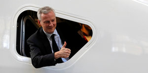 Frankreichs Finanzminister Bruno Le Maire guckt auf einem Flugzeug und zeigt Daumen hoch