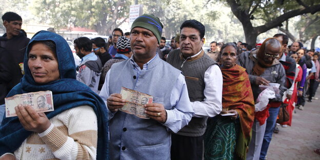 Indische Frauen und Männer stehen, wertlose Banknoten haltend, in einer Schlange Indische Frauen und Männer stehen, wertlose Banknoten haltend, in einer Schlange