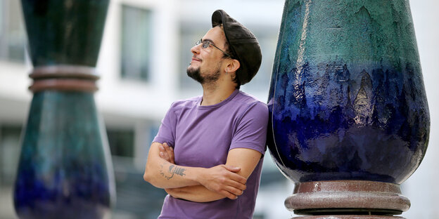 Vanja lehnt mit verschränkten Armen an einer blau und grün lasierten Säule Vanja lehnt mit verschränkten Armen an einer blau und grün lasierten Säule