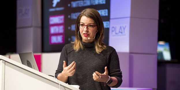 Anita Sarkeesian steht gestikulierend hinterm Rednerpult Anita Sarkeesian steht gestikulierend hinterm Rednerpult