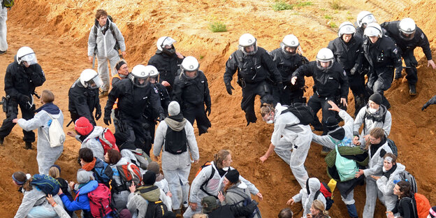 AktivistInnen in weißen Anzügen stehen vor und hinter einer Polizeikette AktivistInnen in weißen Anzügen stehen vor und hinter einer Polizeikette