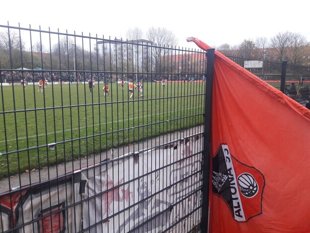 Eine Fan-Fahne von Altona 93 ist auf den Stahlzaun des Stadions gelehnt.