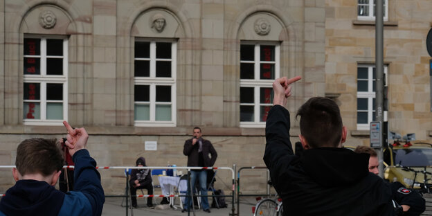 Zwei Menschen zeigen Redner hinter Absperrung ihre Mittelfinger Zwei Menschen zeigen Redner hinter Absperrung ihre Mittelfinger