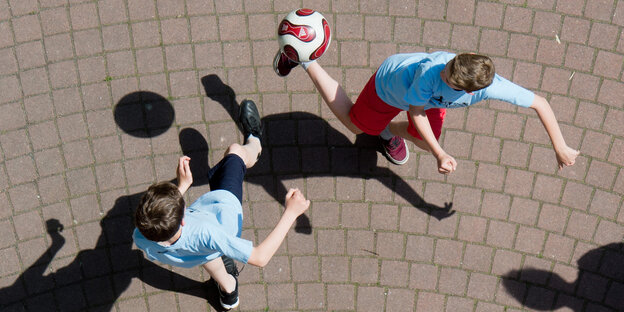 Zwei Jungs tänzeln umeinander und um einen Ball, fotografiert sind sie von oben