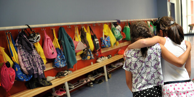 Zwei Schulmädchen gehen Arm in Arm auf eine Garderobe zu Zwei Schulmädchen gehen Arm in Arm auf eine Garderobe zu