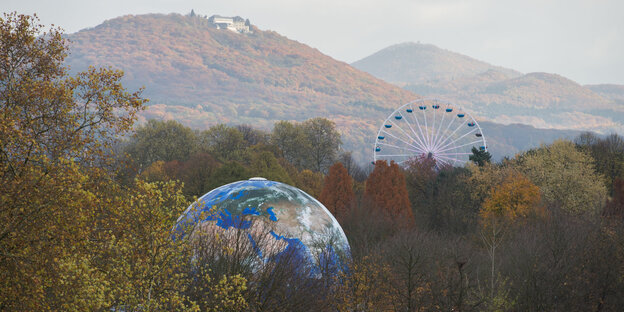 Eine große Weltkugel und ein Riesenrad vor herbstlichen Hügeln Eine große Weltkugel und ein Riesenrad vor herbstlichen Hügeln
