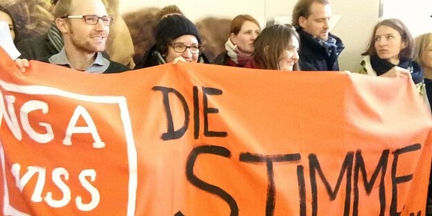 Mehrere jüngere Menschen halten ein oranges Transpi in die Höhe Mehrere jüngere Menschen halten ein oranges Transpi in die Höhe