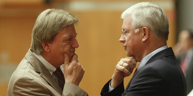 Volker Bouffier und Roland Koch schauen sich fragend an. Sie stützen ihr Kinn auf ihrer Hand ab.