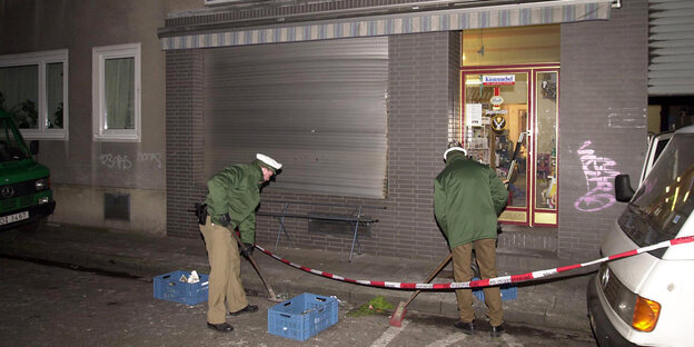 Zwei Polizisten fegen vor einem Laden mit heruntergelassenem Rollo Zwei Polizisten fegen vor einem Laden mit heruntergelassenem Rollo