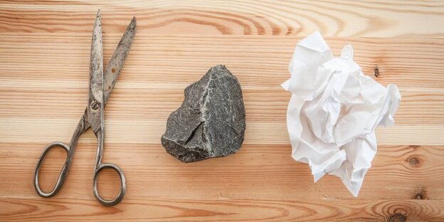 Eine Schere, ein Stein und ein zerknülltes Blatt Papier liegen nebeneinander Eine Schere, ein Stein und ein zerknülltes Blatt Papier liegen nebeneinander