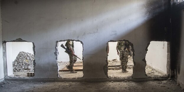 Eine zerstörte Wand. Dahinter die Beine von bewaffneten Soldaten zu sehen, die dort entlanggehen Eine zerstörte Wand. Dahinter die Beine von bewaffneten Soldaten zu sehen, die dort entlanggehen