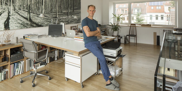 Ein Mann lehnt in einem Arbeitszimmer an einem Schreibtisch Ein Mann lehnt in einem Arbeitszimmer an einem Schreibtisch