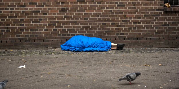 Ein Mensch liegt in einem Schlafsack auf dem Gehweg Ein Mensch liegt in einem Schlafsack auf dem Gehweg