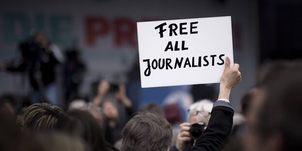 Ein Mensch steht in einer Menschenmenge und hält ein Schild mit der Aufschrift: Free all Journalists Ein Mensch steht in einer Menschenmenge und hält ein Schild mit der Aufschrift: Free all Journalists