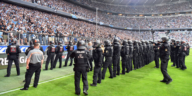 Drei lange Polizeiketten stehen auf dem Rasen des Stadions und schauen in die Ränge der Löwen-Fans von München 1860. Drei lange Polizeiketten stehen auf dem Rasen des Stadions und schauen in die Ränge der Löwen-Fans von München 1860.
