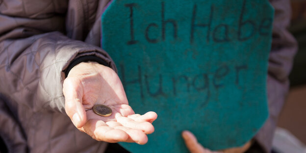 Jemand hält eine Hand auf und in der anderen ein Schild mit der Aufschrift "Ich habe Hunger"