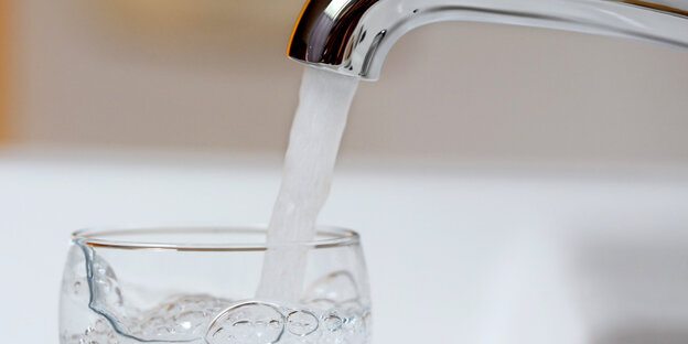 Wasser fließt durch einen Hahn in ein Glas Wasser fließt durch einen Hahn in ein Glas