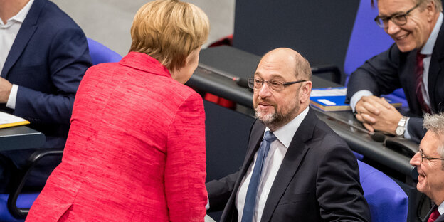 Merkel im magentaroten Sakko steht vor dem sitzenden Martin Schulz, der zu ihr aufsieht Merkel im magentaroten Sakko steht vor dem sitzenden Martin Schulz, der zu ihr aufsieht