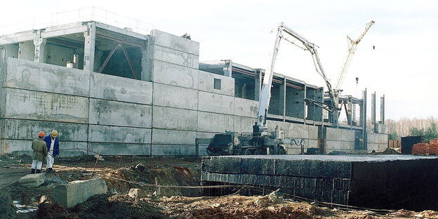 Arbeiter und ein Bagger vor einem Rohbau Arbeiter und ein Bagger vor einem Rohbau