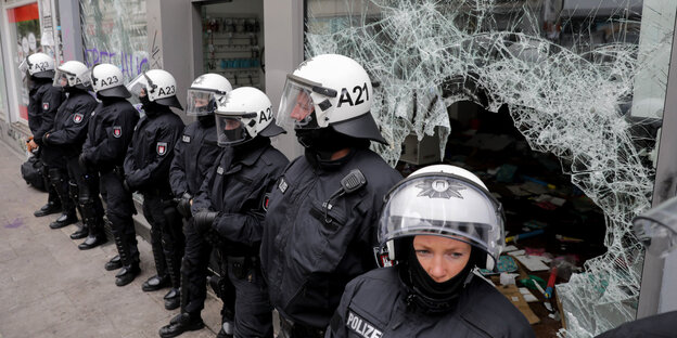 Polizeibeamte mit weißen Helmen stehen vor einer zersplitterten Fensterscheibe Polizeibeamte mit weißen Helmen stehen vor einer zersplitterten Fensterscheibe