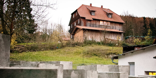 Betonstelen im Vordergrund, ein rustikales Holzhaus im HIntergrund Betonstelen im Vordergrund, ein rustikales Holzhaus im HIntergrund
