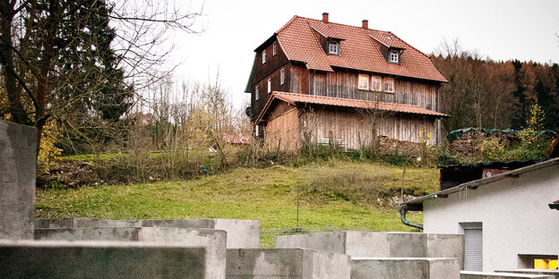 Betonstelen im Vordergrund, ein rustikales Holzhaus im HIntergrund