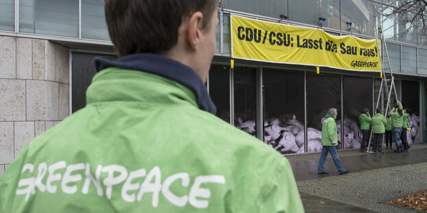 Ein Mann in einer Jacke von Greenpeace vor einen Transparent von Greenpeace Ein Mann in einer Jacke von Greenpeace vor einen Transparent von Greenpeace