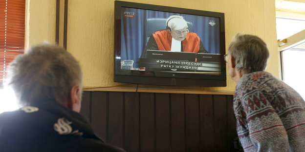 Zwei Menschen schauen auf einen Fersehbildschirm Zwei Menschen schauen auf einen Fersehbildschirm