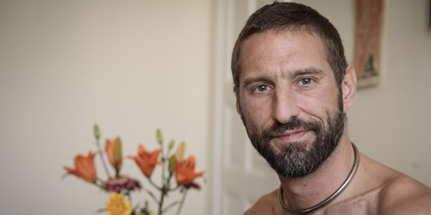 Ein Mann mit einer Ringkette, im Hintergrund orangefarbene Blumen Ein Mann mit einer Ringkette, im Hintergrund orangefarbene Blumen