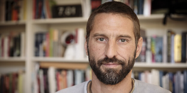 Ein Mann mit Bart vor einem Bücherregal Ein Mann mit Bart vor einem Bücherregal