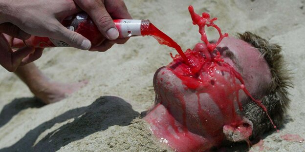 Jemand liegt am Strand und wird mit einem alkoholischen Getränk begossen Jemand liegt am Strand und wird mit einem alkoholischen Getränk begossen