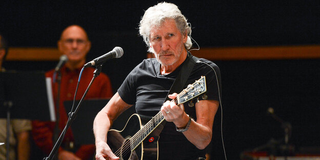 Ein älterer Mann mit grauen Haaren spielt Gitarre vor einem Mikrofon Ein älterer Mann mit grauen Haaren spielt Gitarre vor einem Mikrofon