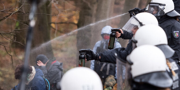 Polizisten versprühen Pfefferspray auf Menschen in einem Wald