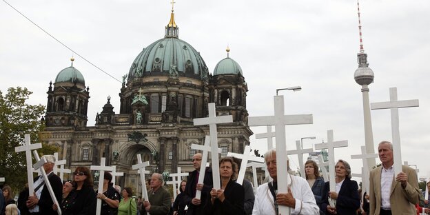 Im Vordergrund viele Menschen, die alle ein weißes Kreuz vor sich hertragen, im Hintergrund der Berliner Dom und der Fernsehturm Im Vordergrund viele Menschen, die alle ein weißes Kreuz vor sich hertragen, im Hintergrund der Berliner Dom und der Fernsehturm