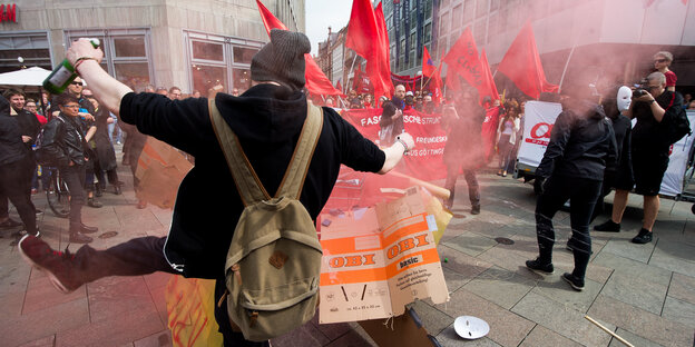 Bei einer Demo tritt ein vermummter Mann mit Bier in der Hand einen Gegenstand weg Bei einer Demo tritt ein vermummter Mann mit Bier in der Hand einen Gegenstand weg