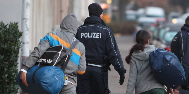 Zwei Polizisten führen zwei Personen zu einem Polizeiwagen