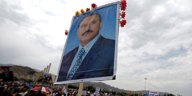 Vor einer Menschenmasse wird ein Plakat mit dem Porträt des ehemaligen jemenitischen Präsidenten Ali Abdullah Saleh hochgehalten. Vor einer Menschenmasse wird ein Plakat mit dem Porträt des ehemaligen jemenitischen Präsidenten Ali Abdullah Saleh hochgehalten.