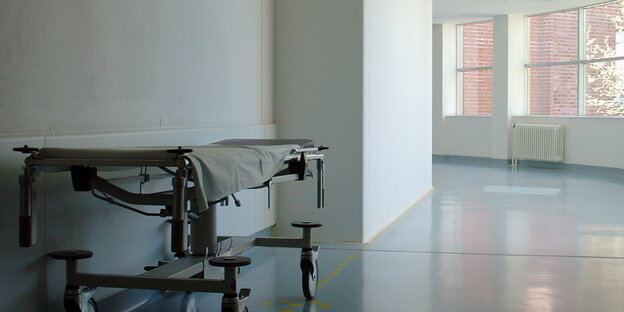 Eine Liege steht im weißen Krankenhausflur, im Hintergrund Fenster Eine Liege steht im weißen Krankenhausflur, im Hintergrund Fenster
