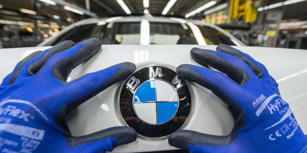 Behandschuhte Hände montieren ein BMW-Emblem auf ein Auto Behandschuhte Hände montieren ein BMW-Emblem auf ein Auto
