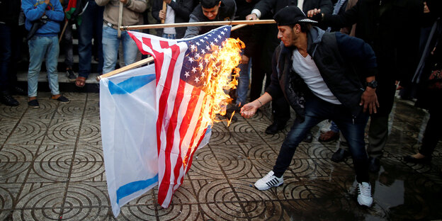 Menschen verbrennen auf einem Platz eine US-Flagge und eine israelische Flagge Menschen verbrennen auf einem Platz eine US-Flagge und eine israelische Flagge