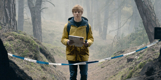 Ein junger Mann mit einer Taschenlampe und einer Landkarte steht alleine auf einem Waldpfad, der mit blau-weißem Flatterband abgesperrt ist Ein junger Mann mit einer Taschenlampe und einer Landkarte steht alleine auf einem Waldpfad, der mit blau-weißem Flatterband abgesperrt ist