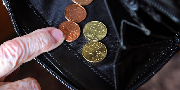 Eine alte Frau sieht in eine Geldbörse, in der sich nur wenige Cent befinden Eine alte Frau sieht in eine Geldbörse, in der sich nur wenige Cent befinden