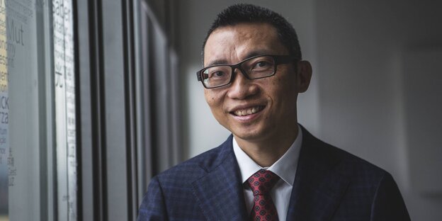 Ein chinesischer junge Mann mit Brille und Anzug an einem Fenster Ein chinesischer junge Mann mit Brille und Anzug an einem Fenster