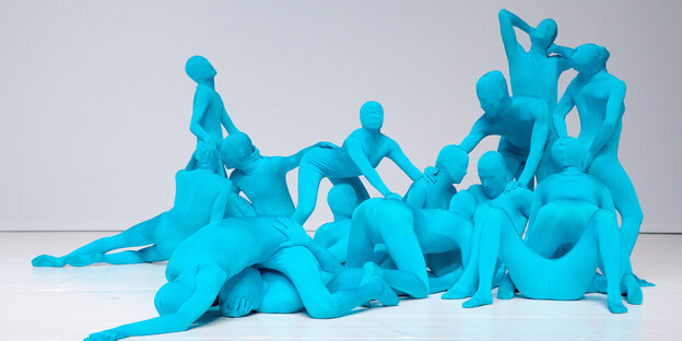 Mehrere ineinander verschlungene Tänzer*innen in blauen Ganzkörperanzügen Mehrere ineinander verschlungene Tänzer*innen in blauen Ganzkörperanzügen