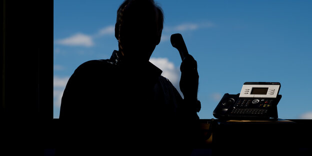 Ein Mann mit einem Hörer in der Hand vor einem Fenster, als Silhouette Ein Mann mit einem Hörer in der Hand vor einem Fenster, als Silhouette