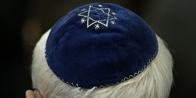 Ein grauhaariger Mann trägt eine blaue Kippa, die mit dem Davidstern bedruckt ist.