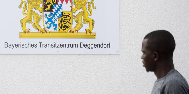 Ein Mann steht neben einem Schild auf dem steht: „Bayerisches Transitzentrum Deggendorf“ Ein Mann steht neben einem Schild auf dem steht: „Bayerisches Transitzentrum Deggendorf“