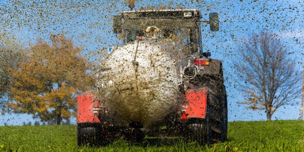 ein Traktor sprengt Gülle auf ein Feld