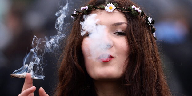 Eine junge Frau mit Blumenkette auf dem Kopf raucht einen Joint. Eine junge Frau mit Blumenkette auf dem Kopf raucht einen Joint.